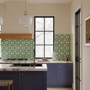 Boho-chic kitchen interior with Colamo dark green and orange geometric peel and stick backsplash tiles, featuring a navy blue island and marble countertops.