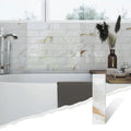 Colamo elongated Calacatta Gold peel and stick subway tile installed as a glossy marble bathroom wall behind a freestanding tub, with a single tile shown in the corner