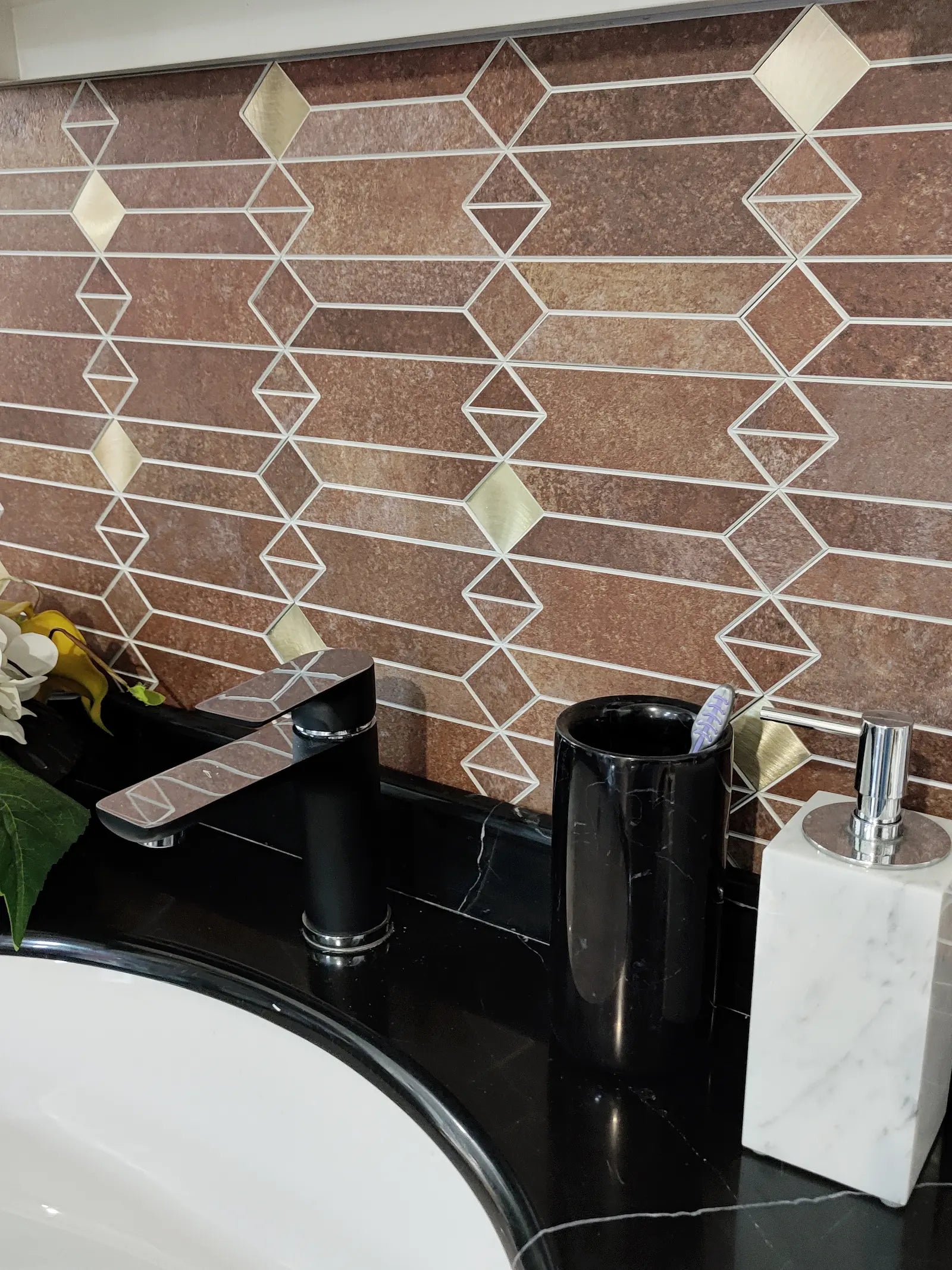 Mid-century geometric peel and stick backsplash tile above a black countertop sink with a faucet and soap dispenser